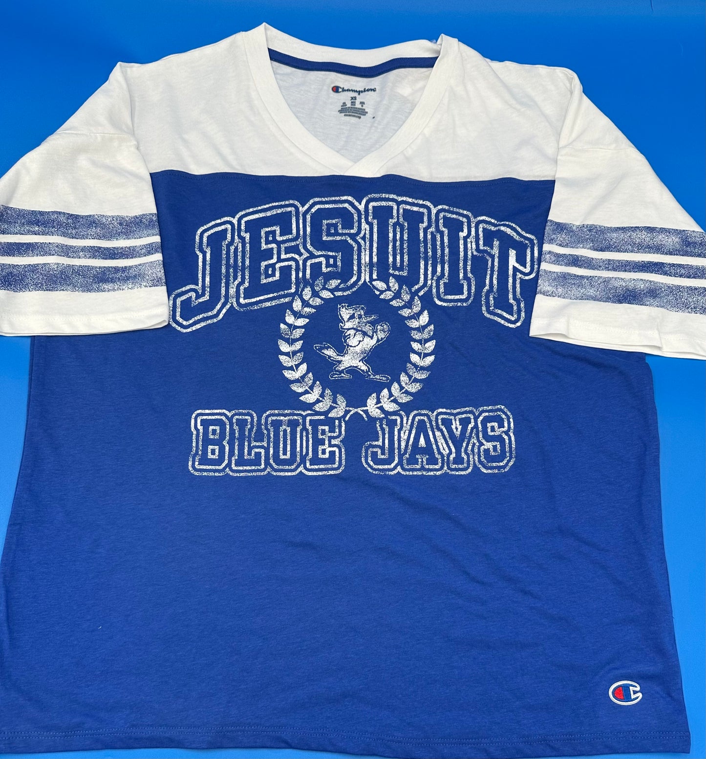 Champion. From the 2024 Stadium Collection. 60% Cotton/40% Polyester. Royal Blue Heather and White. Set in sleeves. Relaxed fit. Shorter length. This top is oversized. Definitely side down at least ONE size when ordering. Distressed royal blue stripes on sleeves with distressed Jesuit Blue Jays with Jayson logo.