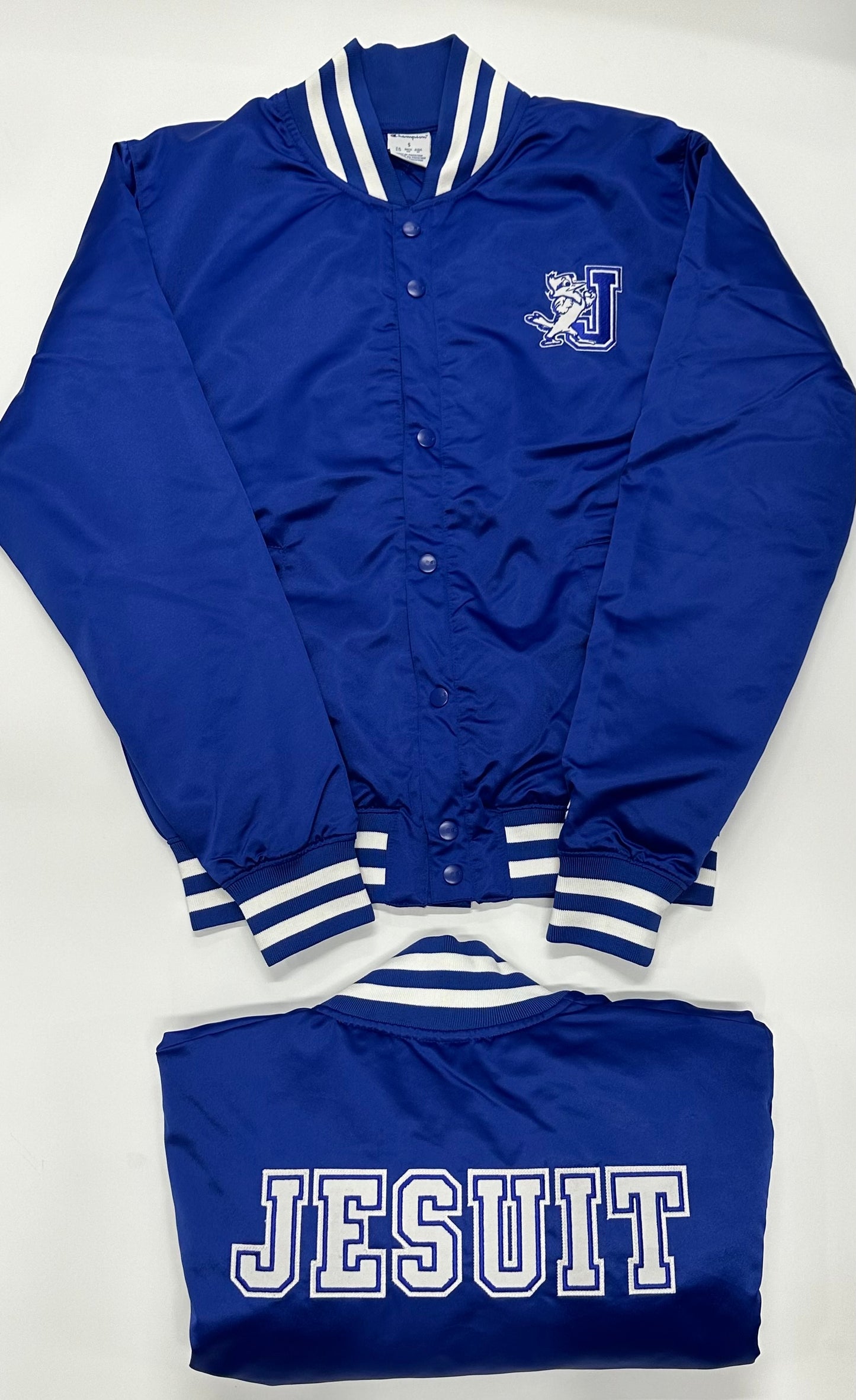 Champion.
100% Polyester Satin.
This Satin Bomber Jacket is a modern twist on the vintage varsity style. The jacket features a striped stand-up collar, cuffs and waistband. Jayson/J logo at left chest, and JESUIT displayed on the jacket's backside. Quilted lining. Wear it when you want to show off your Blue Jay spirit.