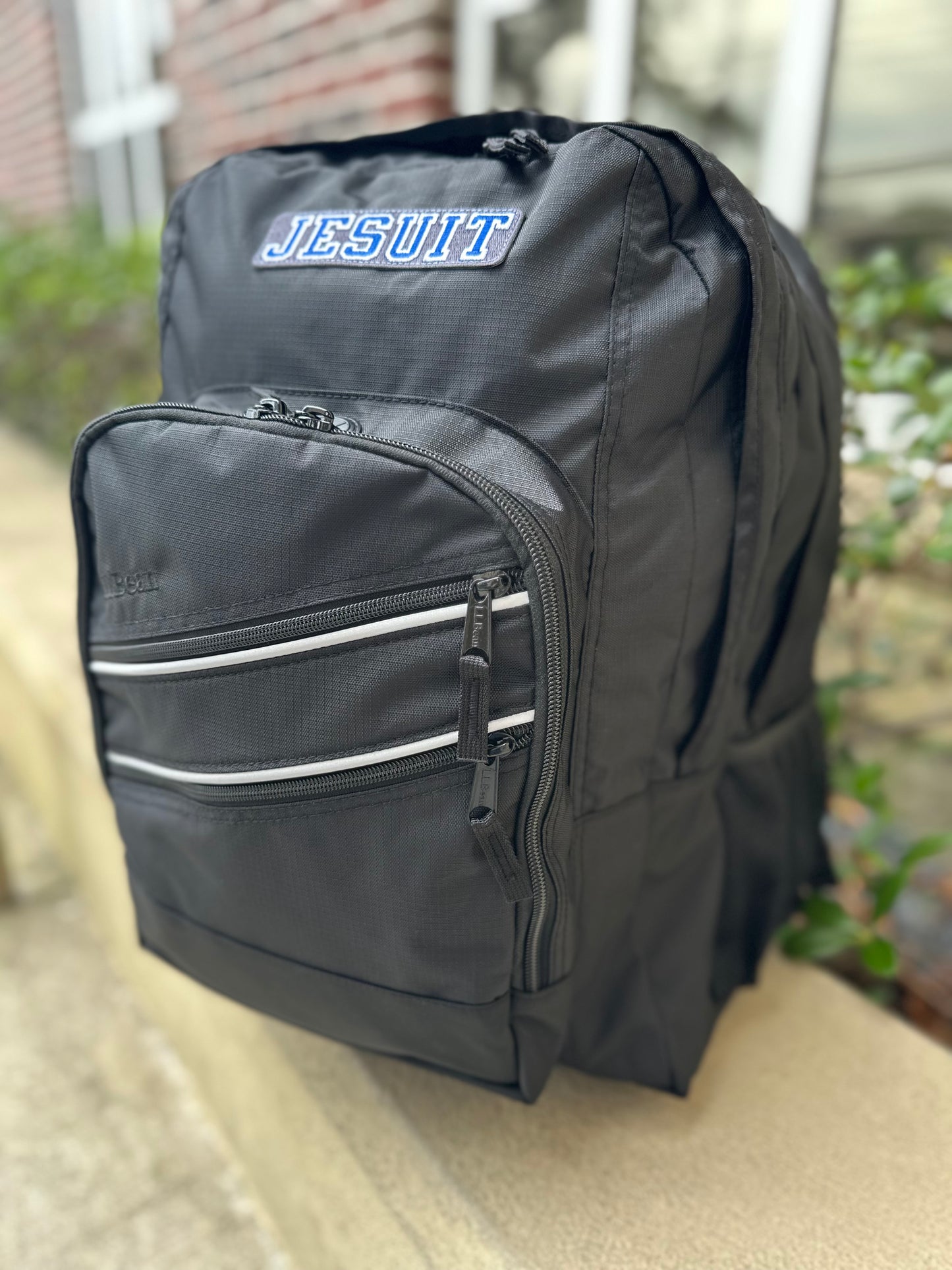 L L Bean.
Super Deluxe Size.Dimensions 17 1/2"H x 13 1/4"W x 13 1/4"D
420-denier ripstop nylon.Spot clean.3M Scotchlite reflective piping on front and straps for 360-degree visibility. Haul loop on top of bag.
Duel main compartments with an organizer panel to keep things handy.Unpadded storage sleeve for folders. Fleece lined interior stash pocket. Two side mesh water bottle holders (can accommodate either size Jesuit water bottles). Padded, adjustable, ergonomically curved straps. JESUIT logo.