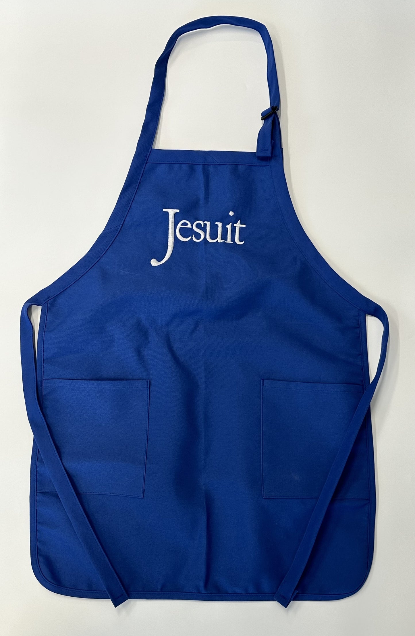 Augusta. Royal Blue. One Size. 65% polyester/35% cotton twill. 1" wide neck strap with slider adjustment. 1" wide waist ties reinforced at stress points. Two patch pockets Rounded bottom with self-fabric binding. 22" width x 30" length. Embroidered Jesuit logo.