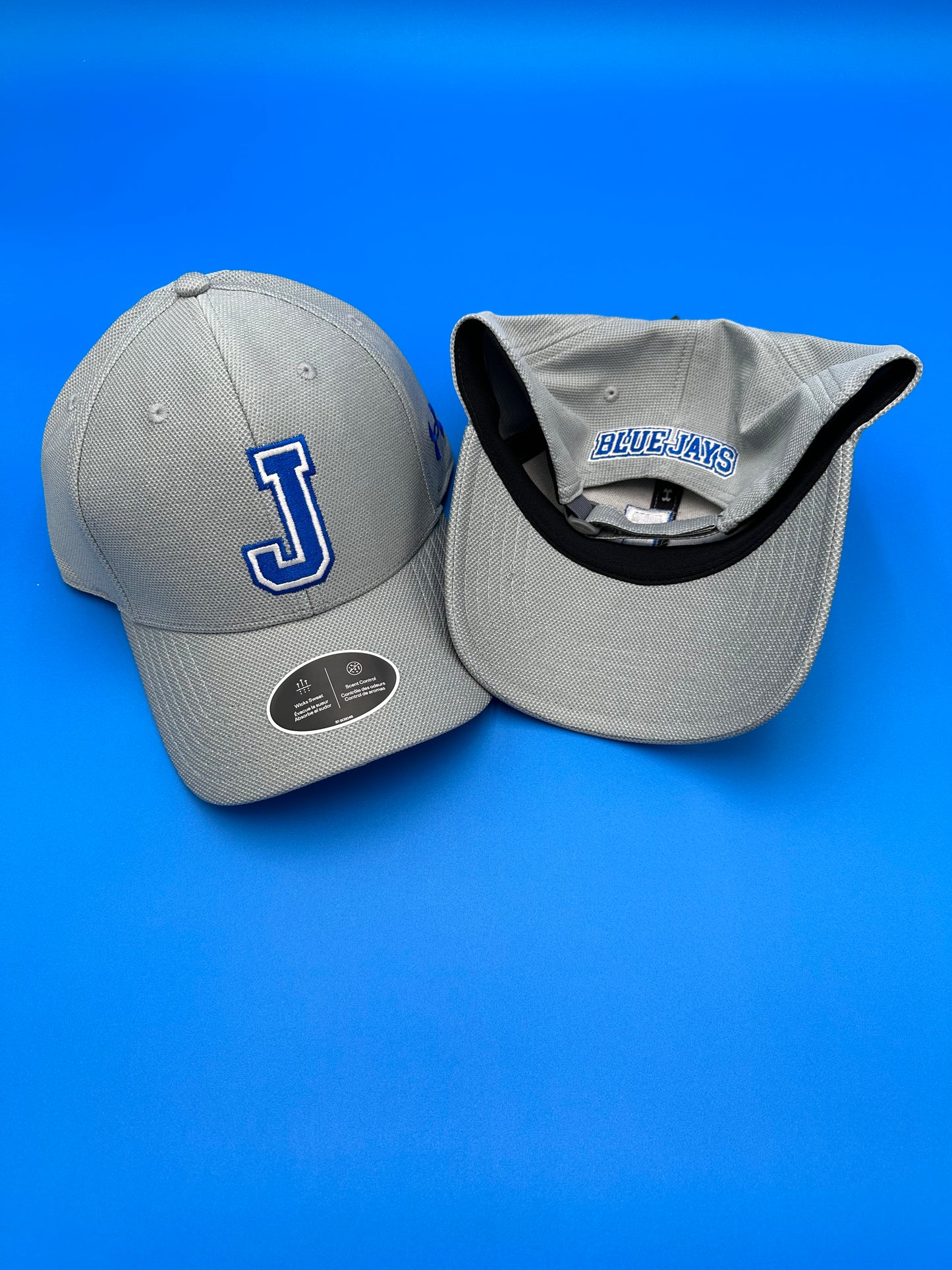 Under Armour. 100% Polyester. Structure w/higher crown. Velcro adjustable closure. One Size Fits All. Steel Heather - J w/Blue Jays on back.