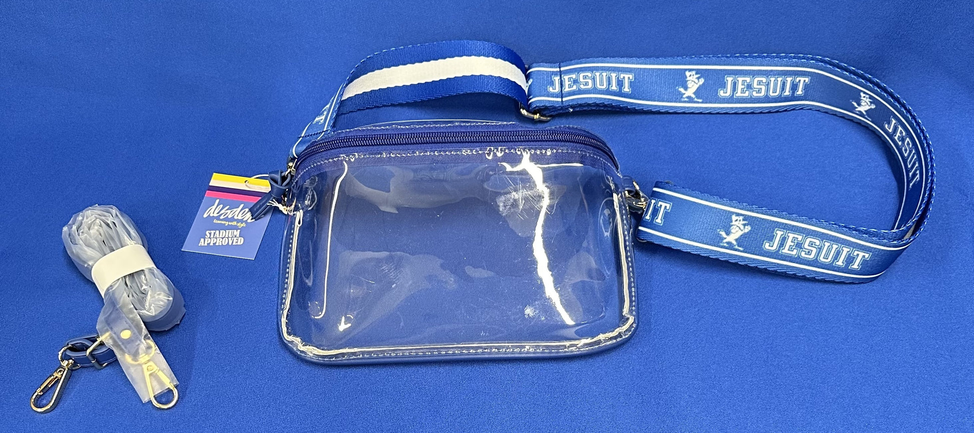 Desden.  9.25"/6"/2.5" dimensions.  Stadium approved.  Clear Plastic Bag - "Sling Style" with Jesuit 1.5" purse straps.  Clear bag with vegan leather trim, zipper closure and removable straps.  Comes with 2 sets of adjustable purse straps, one in matching vegan leather, a 2nd one is Royal Blue/White stripe on one side with JESUIT and Jayson logo on the other.