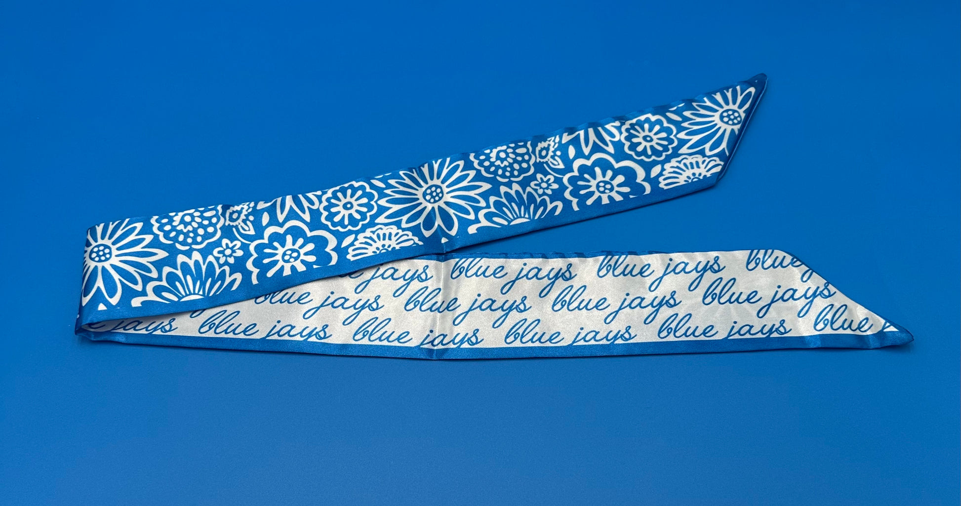 Desden.

100% Polyester.

Measures 36" long x 2.75" wide. Features a floral pattern on one side and our Blue Jays script logo on the reverse. Can be styled around your neck, wrist, hat or purse for effortless, versatile flair.