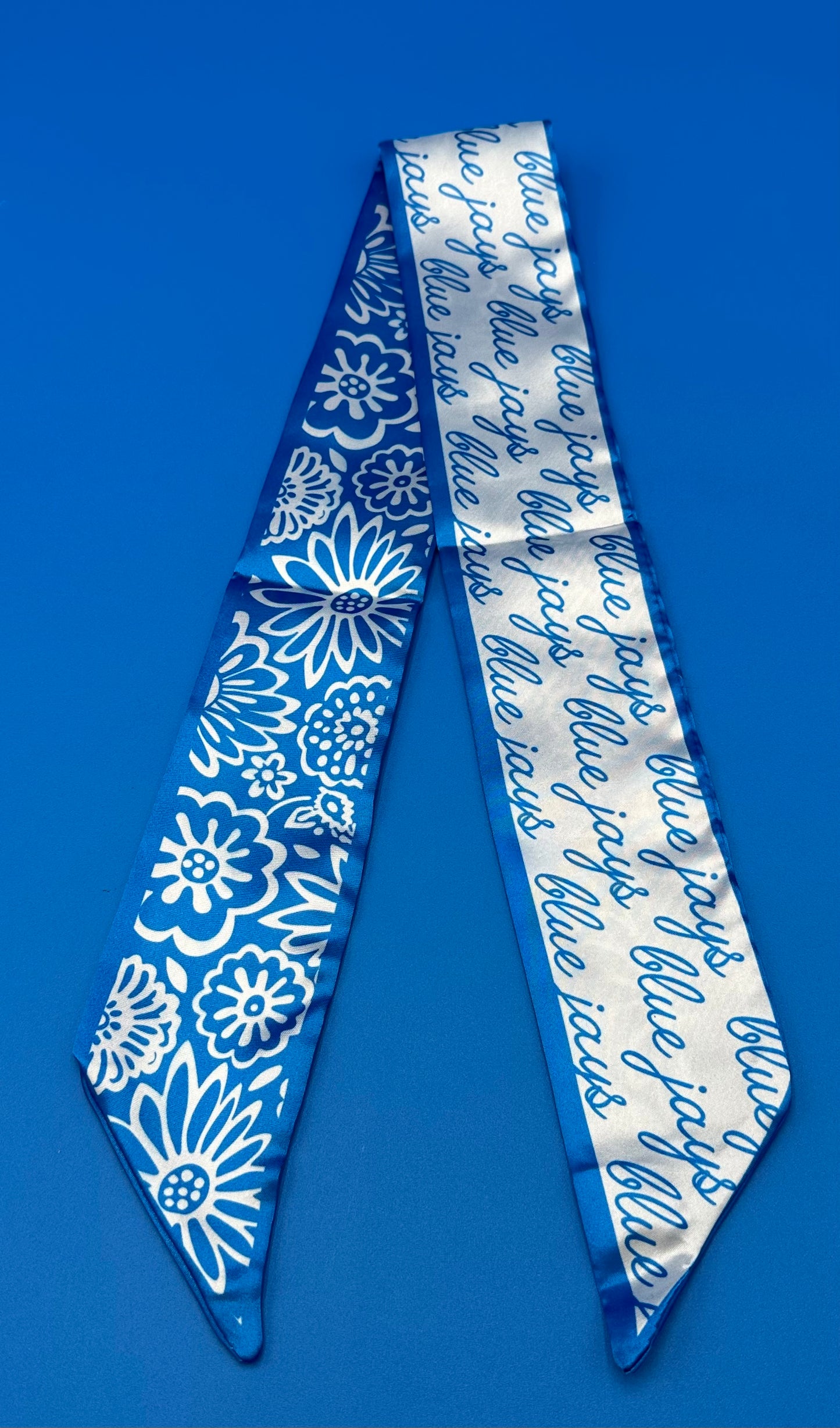 Desden.

100% Polyester.

Measures 36" long x 2.75" wide. Features a floral pattern on one side and our Blue Jays script logo on the reverse. Can be styled around your neck, wrist, hat or purse for effortless, versatile flair.
